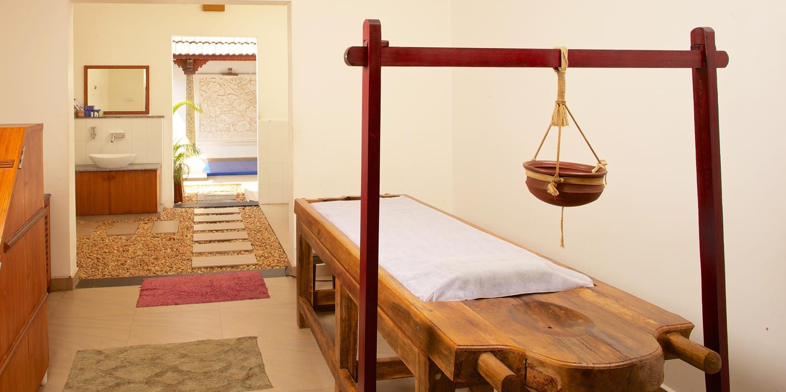 Ayurvedic treatment room with a traditional wooden massage table and hanging oil pot