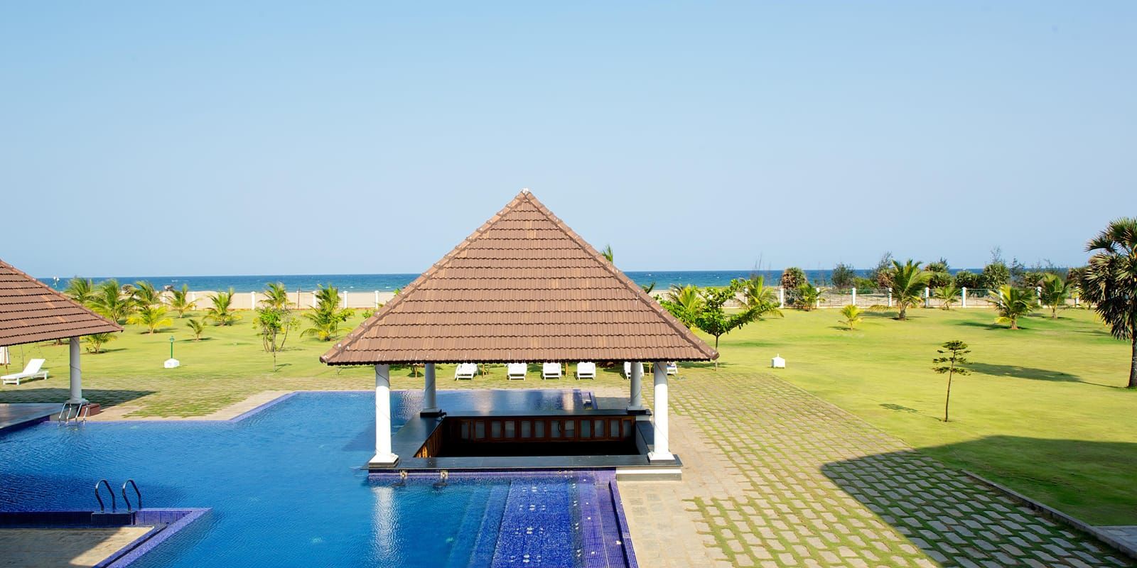 Sunken Bar thatched-roof pavilion in the blue-tiled swimming pool beside the lawn and sea