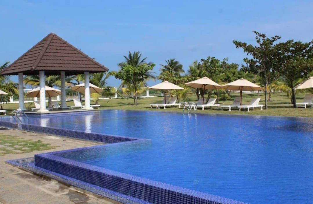 Outdoor swimming pool with blue tiles, thatched-roof gazebos and sun loungers